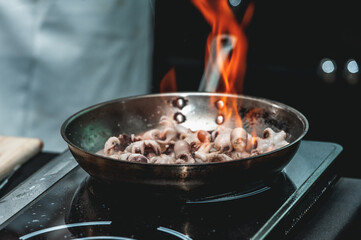 The chef cooks the small octopus on a metal frying pan