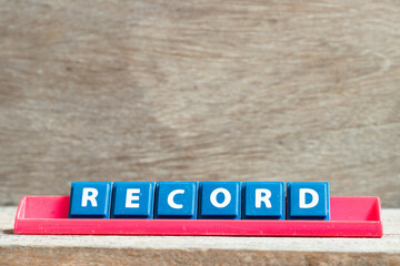 Tile letter on red rack in word record on wood background
