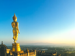 Golden Buddha statue on Wat Phra That Khao Noi view point, Nan, Thailand, Famous landmark of golden buddha image on the top of mountain with morning blue sky background