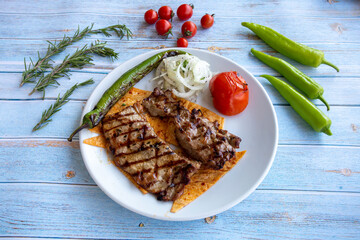 Sirloin steak on blue wooden background - with roasted tomatoes, onions and peppers
