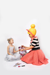 A woman in a bright fancy dress doll costume paints the nails of a little girl princess in a white dress.