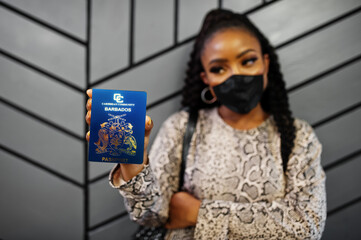 African american woman wearing black face mask show Barbados passport in hand. Coronavirus in America country, border closure and quarantine, virus outbreak concept.