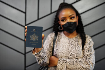 African american woman wearing black face mask show Saint Lucia passport in hand. Coronavirus in America country, border closure and quarantine, virus outbreak concept.