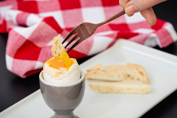 Desayuno tradicional con huevo pasado por agua, mojando el pan en la yema de huevo, con tenedor en la mano