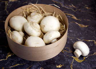 white champignons in a wooden basket on a black marble background