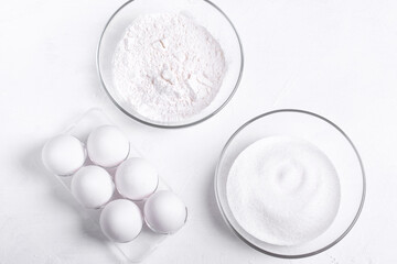 Ingredients to make sponge cake. Eggs, sugar and flour on the white table. Step by step recipe of sponge cake. Step 1.  Set of white ingredients. Top view