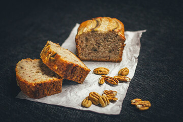 Slices of banana bread on rustic paper, accompanied by raw nuts.