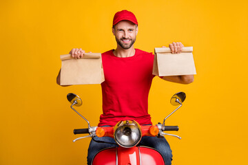 Photo of cheerful guy ride bike hold two paper packages wear red t-shirt headwear isolated yellow...