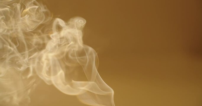 Close up white smoke curling on yellow orange background slow motion. Vapor steaming from incense stick cigarette or hot water copy space text. Moving wallpaper abstract tranquility zen meditation