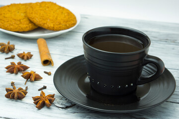 A cup of coffee, cinnamon, star anise, cloves and cookies on the table. Composition with coffee.