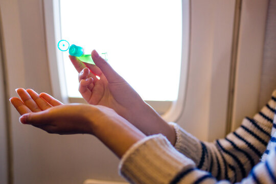 little girl applying sanitizer gel onto her hand while sitting on plane for protection against infectious virus and germs window porthole background