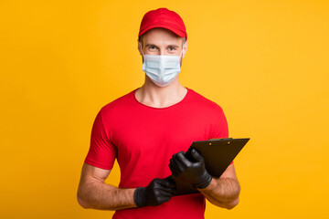 Photo of young courier man hold clipboard take order wear mask red t-shirt cap isolated yellow...