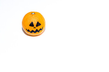 Ripe mandarin, orange yellow tangerine with black scary face on white background. Halloween concept