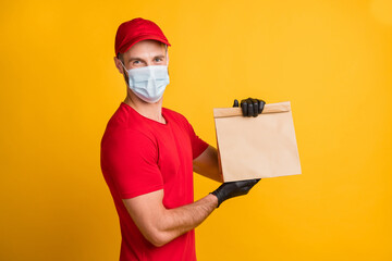 Fototapeta na wymiar Photo of delivery guy hold takeaway package look camera wear mask red t-shirt cap isolated yellow color background