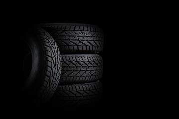Stack of four new black tyres for winter car on black background