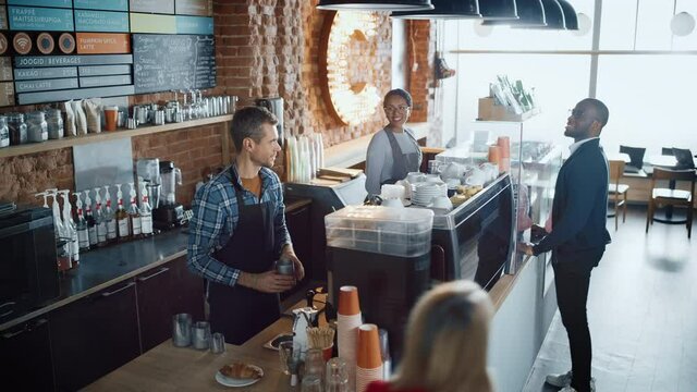Latin Female Cashier and Male Barista in Checkered Shirt Accept Orders from Diverse Clients in Coffee Shop Bar. African American Handsome Customer Orders Take Away Latte from a Cozy Lifestyle Cafe.