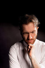 Fototapeta premium A man on a black background in a white shirt. Thinking about something.