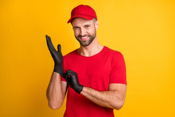 Photo of cheerful bearded guy put on black latex glove wear red t-shirt headwear isolated yellow...