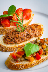Crostini with meat sauce, tomatoes, basil and peppers on a white plate