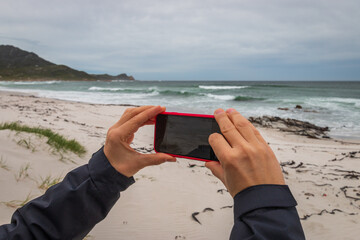 Woman taking a picture with a smart phone at a Platboom beach, South Africa.
