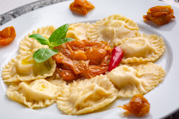 Closeup of tasty appetizing ravioli with yellow tomato and basil on white plate