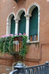Fototapeta na wymiar Venise, Italie, 27 février 2014 : Façade rouge, fênetres mauresques et un balcon avec plantes susspendues dans les ruelles de Venise