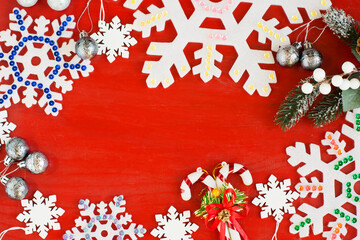 Decorative snowflakes and a spruce branch on a red wooden background.