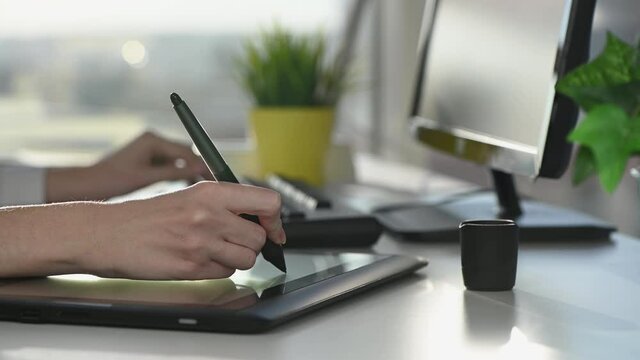 woman designer draws with stylus on tablet in office at table on sunny day