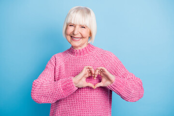 Photo portrait of cheerful elderly woman showing heart with fingers on chest isolated on pastel blue colored background