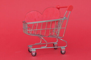 close-up of a small cart from a supermarket with a red heart on a red background. Horizontal photo