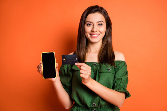 Photo of adorable lady dressed green off-shoulders blouse holding credit card modern gadget isolated orange color background