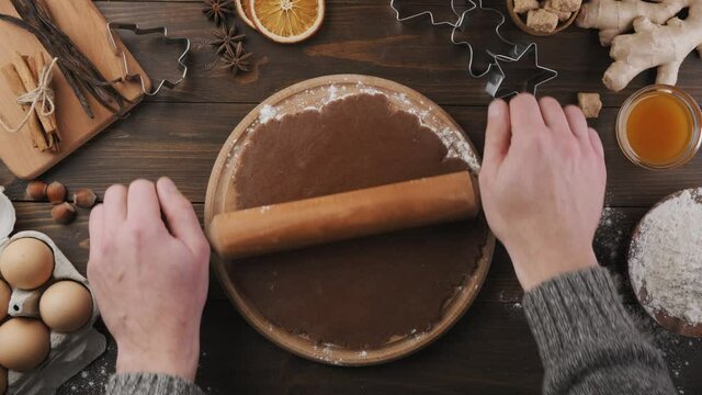 Baker's hand making dough for festive cookies on a wooden table, top view. Roll out the dough with a rolling pin, ingredients for Christmas baking.