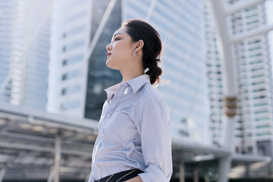 A beautiful Asian business woman is walking in a business district with a look of having been succeeded.