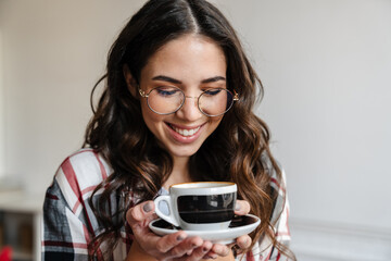 Happy nice brunette woman in eyeglasses smiling and drinking coffee