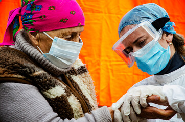 A doctor in a protective suit examines a patient during a coronavirus outbreak. A medic measures the oxygen saturation of an old grandmother during the coronavirus pandemic. Social distancing