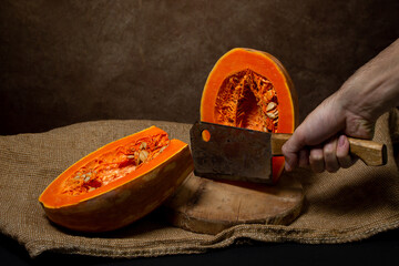 The hand cuts the pumpkin in half with an ax. Long pumpkin. Autumn vegetable.