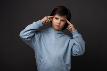 Studio shot of boy 10-12 years old pointing with fingers at head. Concept of thinking. Studio shot, gray background