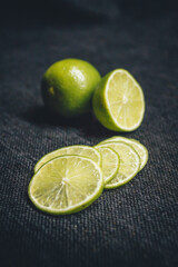 One whole lime, half a lime, and slices of lime on a dark background.