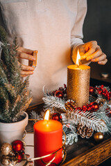 Female Hand lighting candles on decorated table at Christmas. New year burning candle, advent time,...
