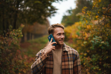 Joyful man talking on mobile phone while strolling in autumn forest
