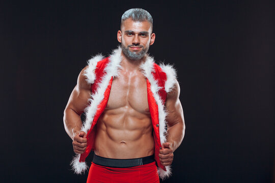 Sexy Santa Claus . Young muscular man wearing Santa Claus hat demonstrate his muscles. Isolated on black background.