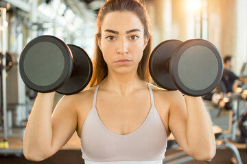 Fototapeta na wymiar Portrait of young woman is sportswear exercising with dumbbells at gym.