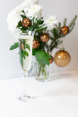 Glass of champagne, Christmas bouquet in glass vase with white chrysanthemum flowers, fir tree branch, golden balls, light garland  on white background