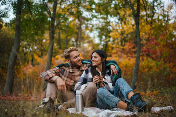 Young happy couple drinking tea and hugging while resting in forest