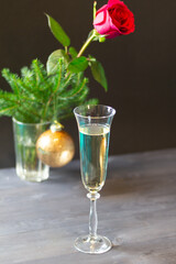Glass with champagne on black background with christmas decoration in vase of fir tree branch, golden ball and red rose