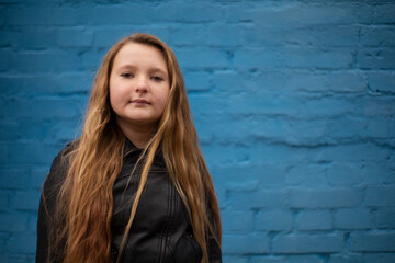 portrait of cute brunette teen girl in Leather Jacket on the background of blue brick wall . Cosiness, fashion, style