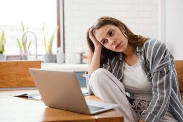 Serious beautiful woman in earphones using laptop while sitting at home