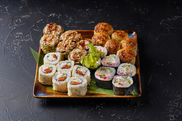 Set of hot roll with eel, Alaska roll with cream cheese, baked sesame roll with crab on a plate with a dark background.