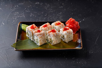 Roll sushi with tiger prawns, cream cheese, cucumber, salmon, eel with sesame seeds and masago roe.  On black background.