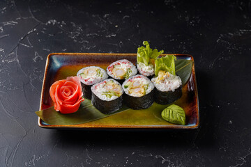 Sushi rolls with shrimp tempura, tobiko roe, cream cheese, cucumber, iceberg lettuce on black background.